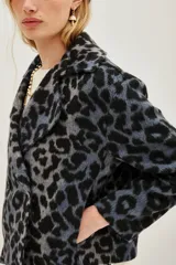 Tapado corto de corte sastre con solapas amplias y cierre frontal cruzado de doble botonadura. Presenta un estampado animal print en tonos grises y negros, con textura suave y mangas largas.