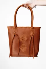 Bolso tipo matera de cuero color marrón, con diseño artesanal grabado en el frente y detalles de costuras cruzadas en las asas.