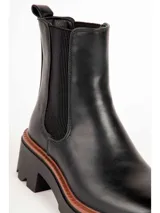 Bota tipo Chelsea de color negro, con elásticos laterales, suela track y taco cuadrado con detalle en tono marrón.