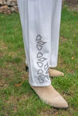 Pantalón blanco de tiro medio con botón y cremallera, detalles de strass en el bajo y corte amplio.