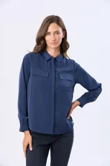 Blusa tipo camisa de manga larga en color azul marino, confeccionada en tela suave y sedosa con doble capa en el frente. Presenta cuello clásico, cierre frontal con botones ocultos y un bolsillo en el pecho.