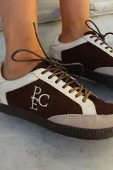 Championes de estilo urbano en combinación de tonos marrones y crema, confeccionados en gamuza y cuero. Presentan cordones jaspeados, suela de goma y detalle de logo bordado en el lateral.