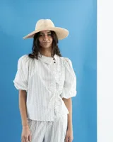 Blusa de denim liviano de corte asimétrico en tono azul, con mangas abullonadas, cuello redondo y cierre lateral con lazos para atar y botones.