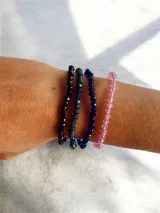 Set de cuatro pulseras elásticas compuestas por cuentas facetadas brillantes en tonos negro, azul oscuro y rosa.