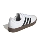 Championes Adidas modelo VL Court, de color blanco con las tres tiras clásicas en negro y suela de goma marrón. Presenta puntera reforzada en gamuza gris claro y cordones blancos.