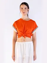Remera color naranja de manga corta, confeccionada en algodón, con detalles de flecos y bordado en las mangas.