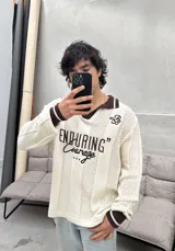 Remera tejida de manga larga con cuello polo marrón, diseño perforado y estampado frontal con la frase "ENDURING Courage".