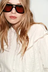 Camisa blanca de cuello redondo con volantes, manga larga con puños elásticos y cierre frontal con botones forrados. Presenta detalles de puntilla y jaretas en el delantero.