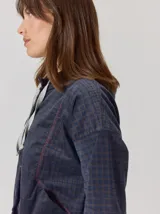 Campera de corte holgado con textura aterciopelada y estampado de cuadros sutil. Presenta cuello con cordones ajustables, cierre frontal con botones y mangas largas con puños elásticos.