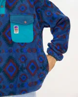 Buzo de polar fleece con diseño estampado geométrico en tonos azules, bordó y verde. Presenta cuello alto con cierre de botones a presión, bolsillo frontal con solapa en contraste y puños elásticos.