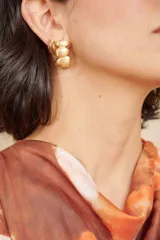 Aros caravanas de diseño irregular en tono dorado con acabado mate, formados por tres piezas redondeadas apiladas en vertical.