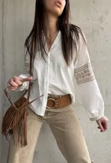 Camisa blanca de calce relajado y tejido liviano, con escote en V y delicados detalles bordados geométricos en tonos tostados en las mangas abullonadas y puños.