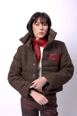 Campera corta con estampado abstracto en tonos marrones y beige, cuello alto, cierre frontal con botones a presión, bolsillos delanteros y bordado negro con las iniciales CP. Forro interior y relleno liviano de guata.