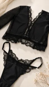 Conjunto de lencería negro de encaje y tul, compuesto por un bralette de manga larga con escote en V y una bombacha tipo tanga con detalles de encaje.