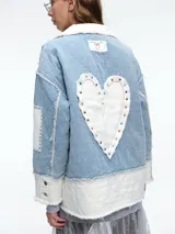 Chaqueta de denim con diseño patchwork, que combina paneles de jean azul claro con secciones de tela blanca acolchada. Presenta solapas amplias, bordes deshilachados, cierre frontal con botones y parches decorativos en las mangas.