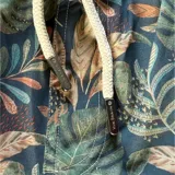 Short de baño con estampado botánico de hojas en tonos verdes y salmón sobre fondo gris azulado. Cuenta con cintura elástica con cordón ajustable, dos bolsillos laterales y un bolsillo trasero.