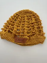 Gorro artesanal tejido a mano en hilo de algodón color mostaza, con diseño de malla abierta (mesh) y etiqueta de cuero con el nombre "Soriame" cosida en el borde.