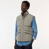 Chaleco acolchado puffer color gris, sin mangas, con cuello alto, cierre frontal de cremallera con solapa de botones a presión y bolsillos laterales amplios.