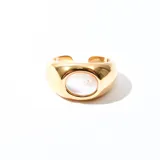 Anillo dorado con una piedra ovalada blanca nacarada en el centro. Es un anillo abierto y ajustable.
