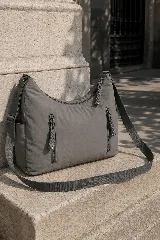 Cartera hobo gris de tela suave y liviana, con bolsillos frontales con cierre y tiradores trenzados, correa ajustable y compartimento principal con cierre.