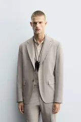 Blazer slim fit de color beige, confeccionada en tejido con lana. Presenta cuello con solapas de muesca, cierre frontal con un botón, bolsillos con solapa en la cadera y bolsillo de vivo en el pecho.