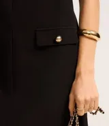 Vestido corto negro de crepé con escote en V tanto en la parte delantera como en la trasera. Tiene bolsillos delanteros con botones dorados.