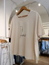 Remerón oversize de algodón color beige, de corte amplio y relajado, con cuello redondo y mangas cortas. Presenta una estampa lineal minimalista en color negro en el centro del pecho, con un diseño de una figura paseando un perro.