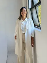 Chaleco largo de punto color crudo, con diseño abierto, sin botones y bolsillos frontales aplicados. Presenta bordes acanalados en la parte frontal y en el ruedo.