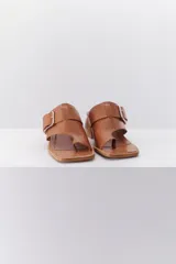 Sandalia color beige con tira ancha de cuero sobre el empeine, hebilla metálica plateada y taco geométrico de madera.