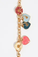 Pulsera de cadena metálica plateada con cierre de mosquetón. Presenta múltiples dijes colgantes en forma de corazón y discos circulares esmaltados en colores rosado, naranja, amarillo, verde y bordó, con el logo de la marca grabado en cada pieza.