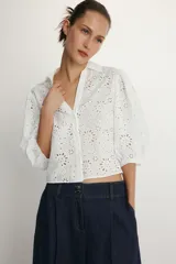 Camisa de cuello solapa y escote en pico, confeccionada en tejido con bordados perforados a tono. Presenta mangas abullonadas por debajo del codo y cierre frontal con botones.