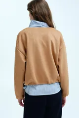 Chaqueta de punto pesado color tostado, con escote redondo, cierre frontal y bolsillos laterales. Presenta un diseño oversized con hombros caídos y terminaciones elásticas en puños y bajo.