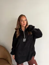 Buzo de corderito color marrón, con cuello alto y cierre frontal parcial. Presenta un diseño holgado con mangas largas y un parche decorativo en el frente.