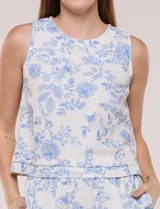 Top crop de lino y viscosa, sin mangas, con escote a la base y estampado floral en tonos azul celeste sobre fondo beige. Cuenta con cierre posterior tipo gota con botón y ruedo recto.