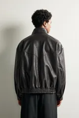 Cazadora relaxed fit de tejido efecto piel en color marrón oscuro con acabado lavado. Cuenta con cuello subido, bolsillos con solapa en la parte frontal, bajo y puños elásticos, y cierre frontal con cremallera y solapa con botones a presión.