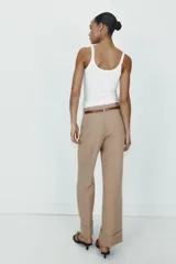 Pantalón de tiro alto color marrón, de corte recto y holgado, con bajo acabado en vuelta. Incluye bolsillos delanteros y cinturón fino a contraste con hebilla metálica.