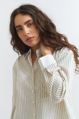 Camisa de manga larga con cuello y puños blancos contrastantes. El cuerpo de la camisa es de color crema con finas rayas verticales azules y tiene un corte crop.
