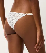 Kit de dos bombachas colaless tipo string confeccionadas en encaje floral, una en color negro y otra en color blanco. Presentan laterales finos regulables con tirantes elásticos y un pequeño dije metálico dorado en la parte frontal.
