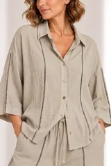 Camisa de lino color beige con cuello camisero, cierre frontal de botones, mangas tres cuartos y detalles de bandas verticales con encaje o calados en el frente y las mangas.