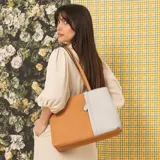 Cartera tipo tote de cuero sintético con diseño combinado en tono gris y blanco, textura granulada, asas largas para el hombro y cierre superior.