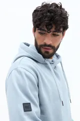 Canguro de algodón color celeste claro, con capucha ajustable mediante cordones trenzados blancos y bolsillo canguro frontal. Presenta un pequeño texto estampado en el pecho.