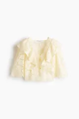 Blusa corta confeccionada en encaje color beige, con escote en V, mangas de longitud francesa y volados amplios que recorren el frente, los hombros y la espalda.