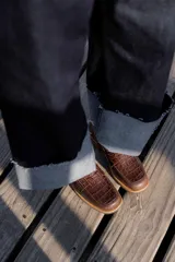 Mocasines negros de cuero con textura tipo cocodrilo en la parte superior y acabado brillante. Presentan una banda frontal clásica y una suela plana con detalle de borde en color natural.