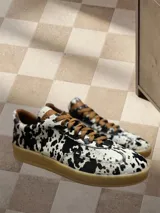 Zapatillas bajas con estampado animal print de vaca en blanco y negro, con cordones marrones y suela color caramelo.
