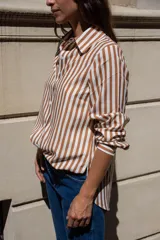 Camisa de corte clásico con estampado de rayas verticales en tonos blanco y marrón. Presenta cuello camisero, cierre frontal con botones y mangas largas con puños rectos. Confeccionada en tela liviana con caída suave.