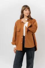 Sobrecamisa de gabardina liviana color crema, con corte oversize, cuello clásico, cierre frontal con botones a presión y dos bolsillos delanteros con solapa.