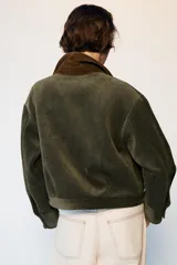 Cazadora de pana marrón con cuello de solapa en color verde oliva a contraste. Presenta cierre frontal de cremallera metálica, mangas largas y dos bolsillos frontales de plastrón con solapa.