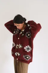 Saco tejido a mano de lana, color bordó con diseño geométrico estampado en tonos gris, blanco y verde. Presenta cuello solapa, cierre frontal con botones grandes y bolsillos delanteros.
