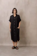 Vestido midi negro con cuello camisero, cierre frontal de botones, bolsillos laterales y mangas cortas con vuelta.