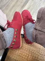 Náuticos de gamuza color rojo con flecos en la parte delantera, cordones al tono y detalle de tachas metálicas en los laterales.